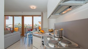 A modern kitchen with a large island, a dining area with a sofa and chairs, and a view of the city through large windows. - Benacus E4 Apartment by Wonderful Italy (Sirmione)
