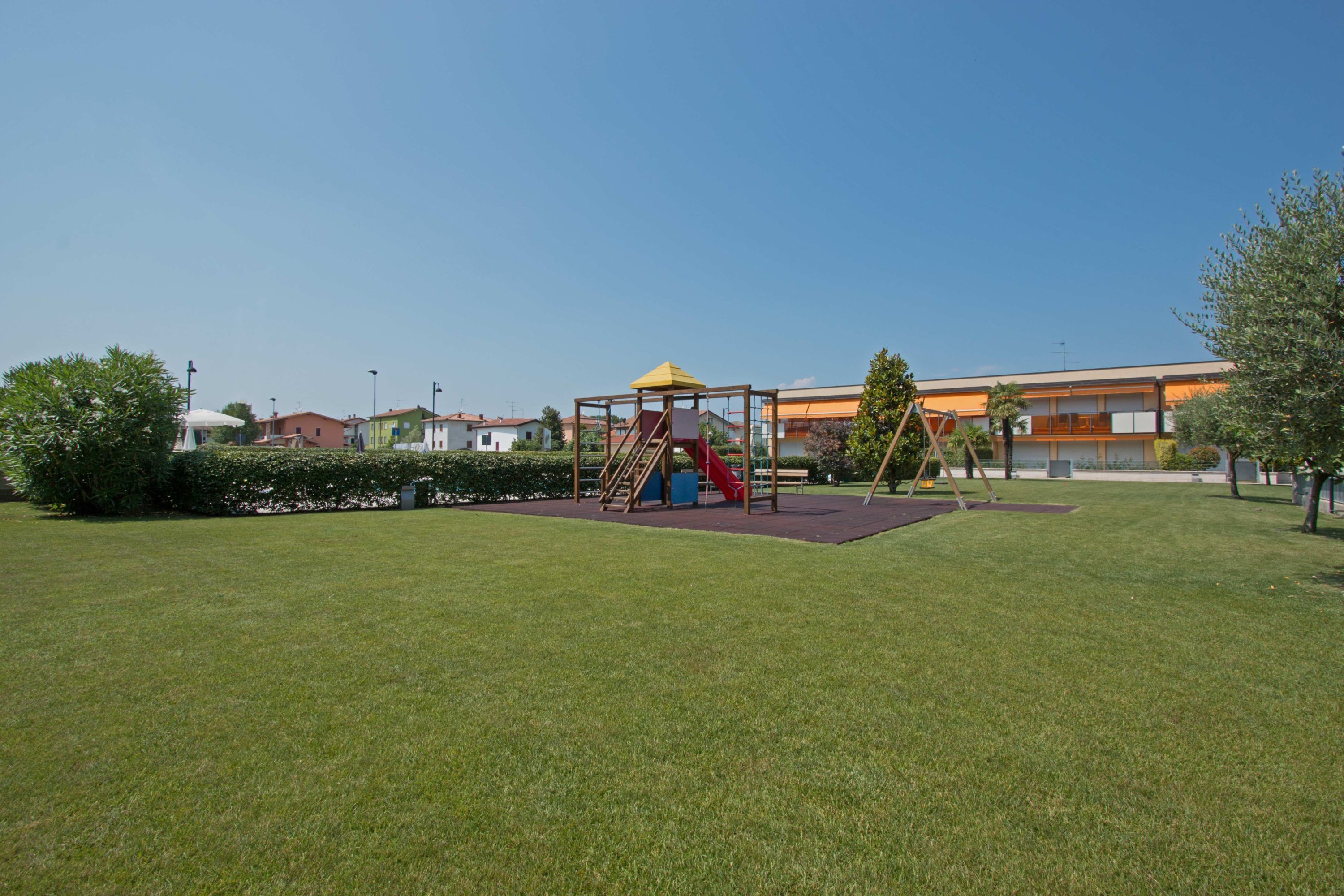 Un parque infantil con un tobogán y una estructura para escalar, rodeado de césped cuidado y árboles.