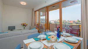 A dining area with a table set for four, a sofa, a TV, and a balcony with a view. - Benacus E4 Apartment by Wonderful Italy (Sirmione)