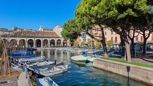 A canal with boats docked, a stone bridge, and buildings with arches. - C era una Volta in Centro by Wonderful Italy (Desenzano del Garda)
