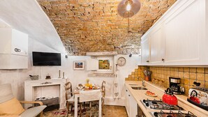 A compact kitchen with a brick ceiling, white cabinets, a dining area with a table and chairs, and a red kettle on the stove. - C era una Volta in Centro by Wonderful Italy (Desenzano del Garda)