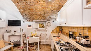 A compact kitchen with a brick ceiling, white cabinetry, a dining area with a table and chairs, and a built-in stove. - C era una Volta in Centro by Wonderful Italy (Desenzano del Garda)