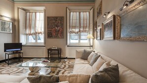 A living room with a sofa, a glass coffee table, a television, and artwork on the walls. - Fancy Apartment in Palazzo Grimaldi by Wonderful Italy (Genoa)