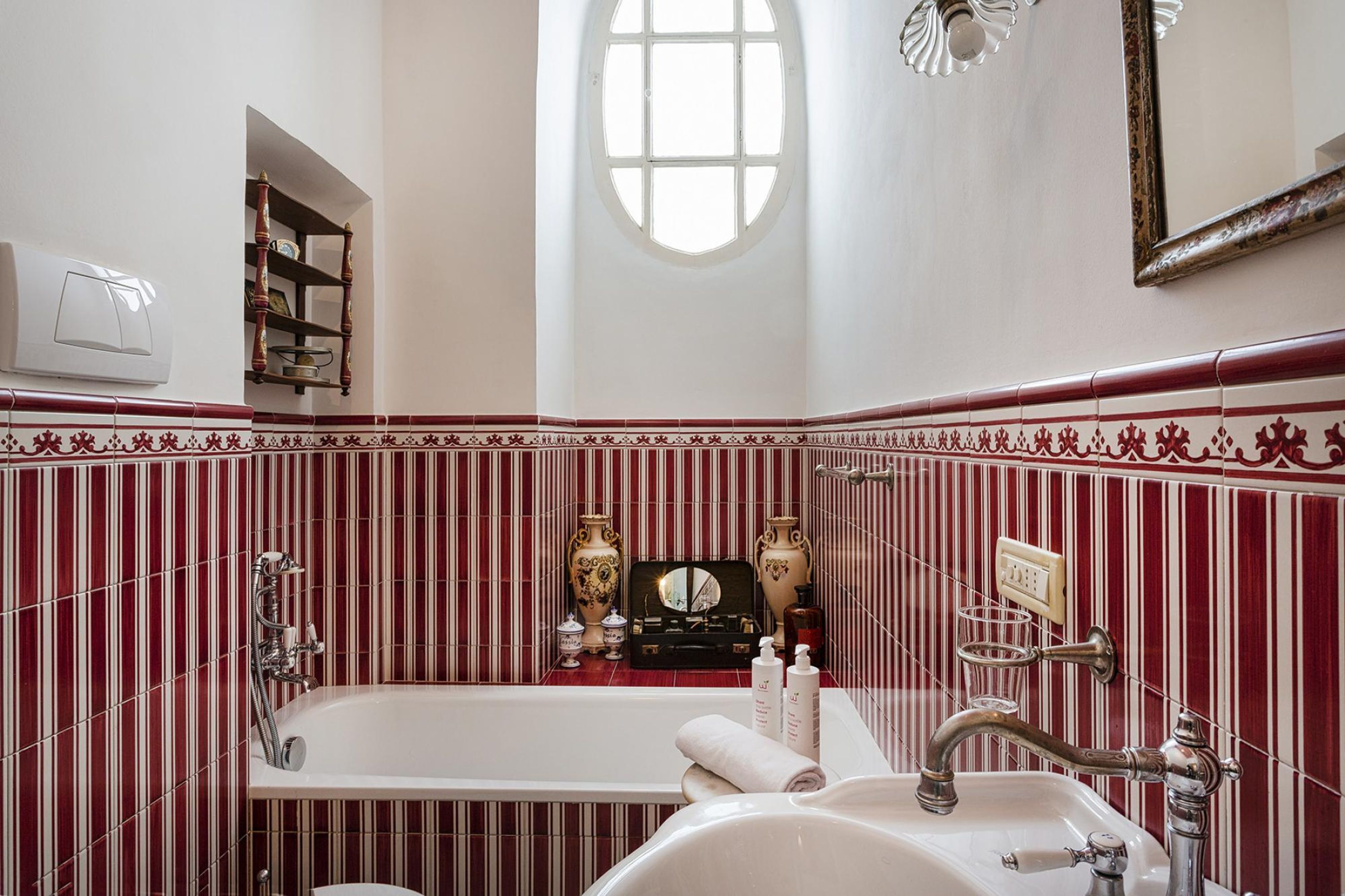 Ein Badezimmer mit einer großen Badewanne, einem Waschbecken und einem Schminkspiegel. Über der Badewanne befindet sich ein Fenster und ein Regal mit Dekoration.