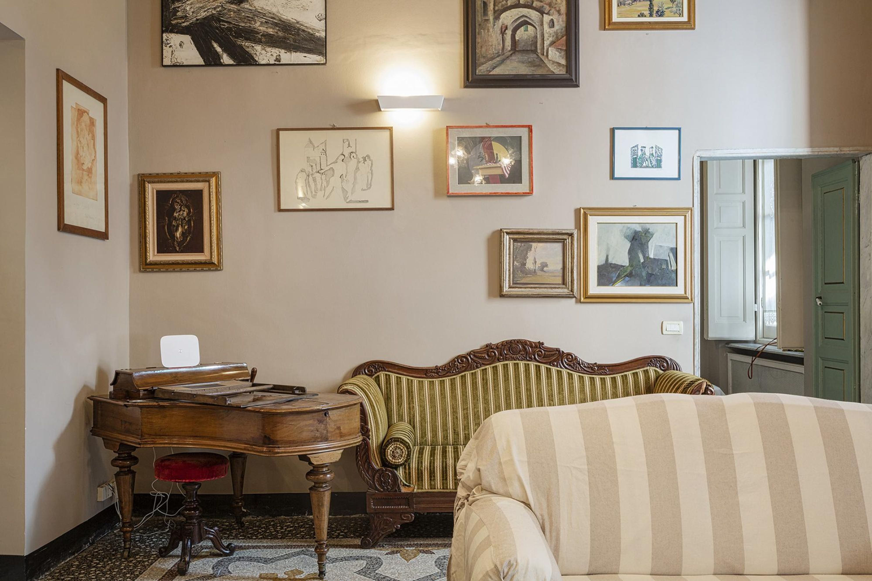 A room with a piano, a sofa, and a bed. There are several framed pictures on the wall.