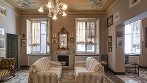 A room with two upholstered chairs, a fireplace, and a chandelier. - Fancy Apartment in Palazzo Grimaldi by Wonderful Italy (Genoa)