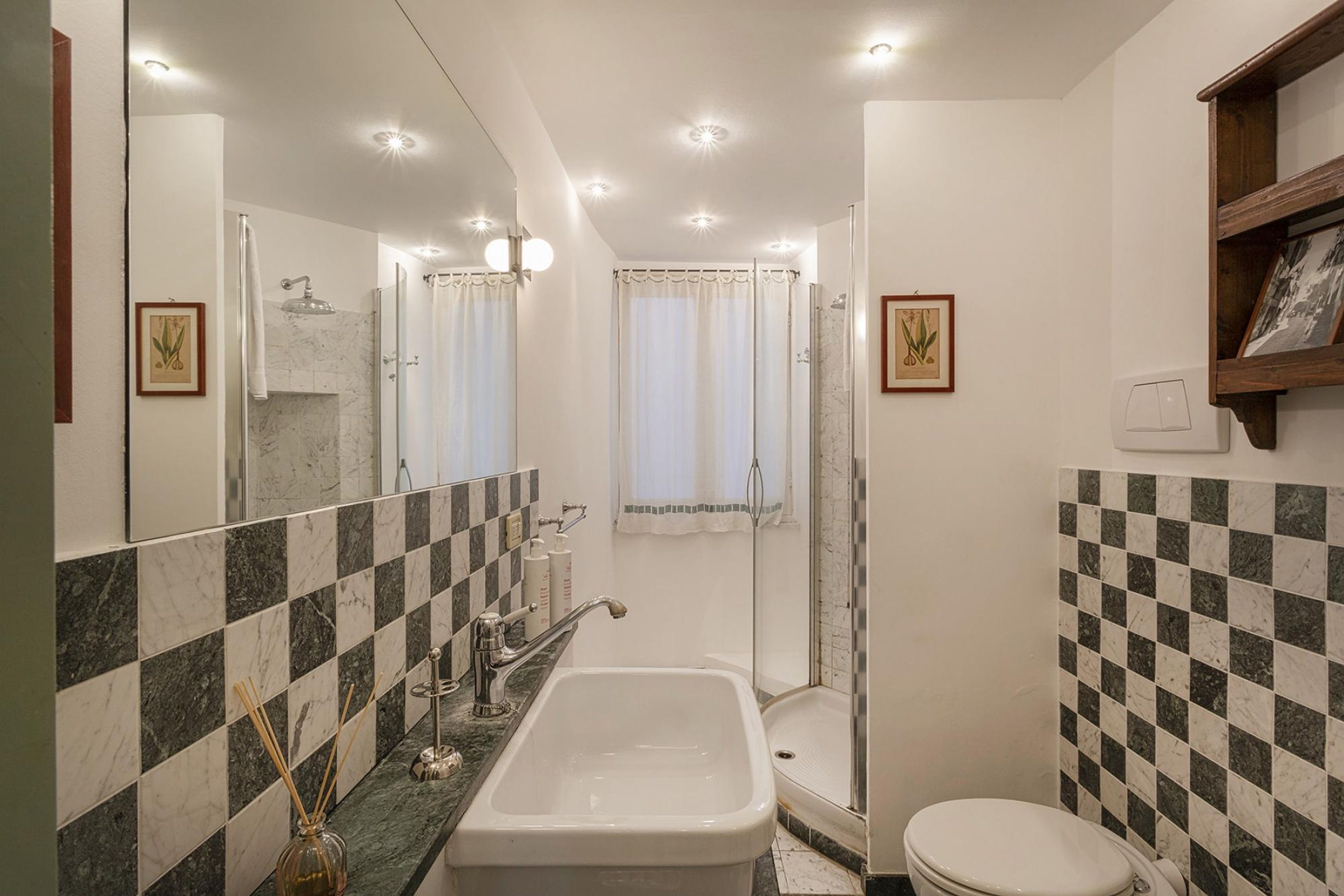 A bathroom with a bathtub, toilet, and shower. It features checkered tile walls and a large mirror.