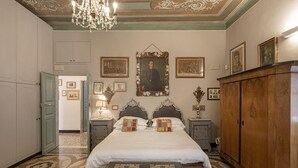 A bedroom with a large bed, two nightstands, a wooden wardrobe, and a chandelier. - Fancy Apartment in Palazzo Grimaldi by Wonderful Italy (Genoa)