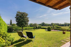 Une pelouse bien entretenue, agrémentée de deux chaises de jardin, d’une pergola en bois et offrant une vue sur un jardin aménagé avec différents arbres et arbustes.