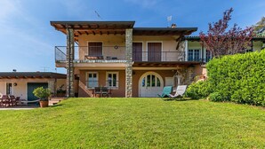 A two-story house with a stone facade, a balcony, and a well-maintained lawn. - Casa Alba con Giardino e Patio by Wonderful Italy (Lonato del Garda)