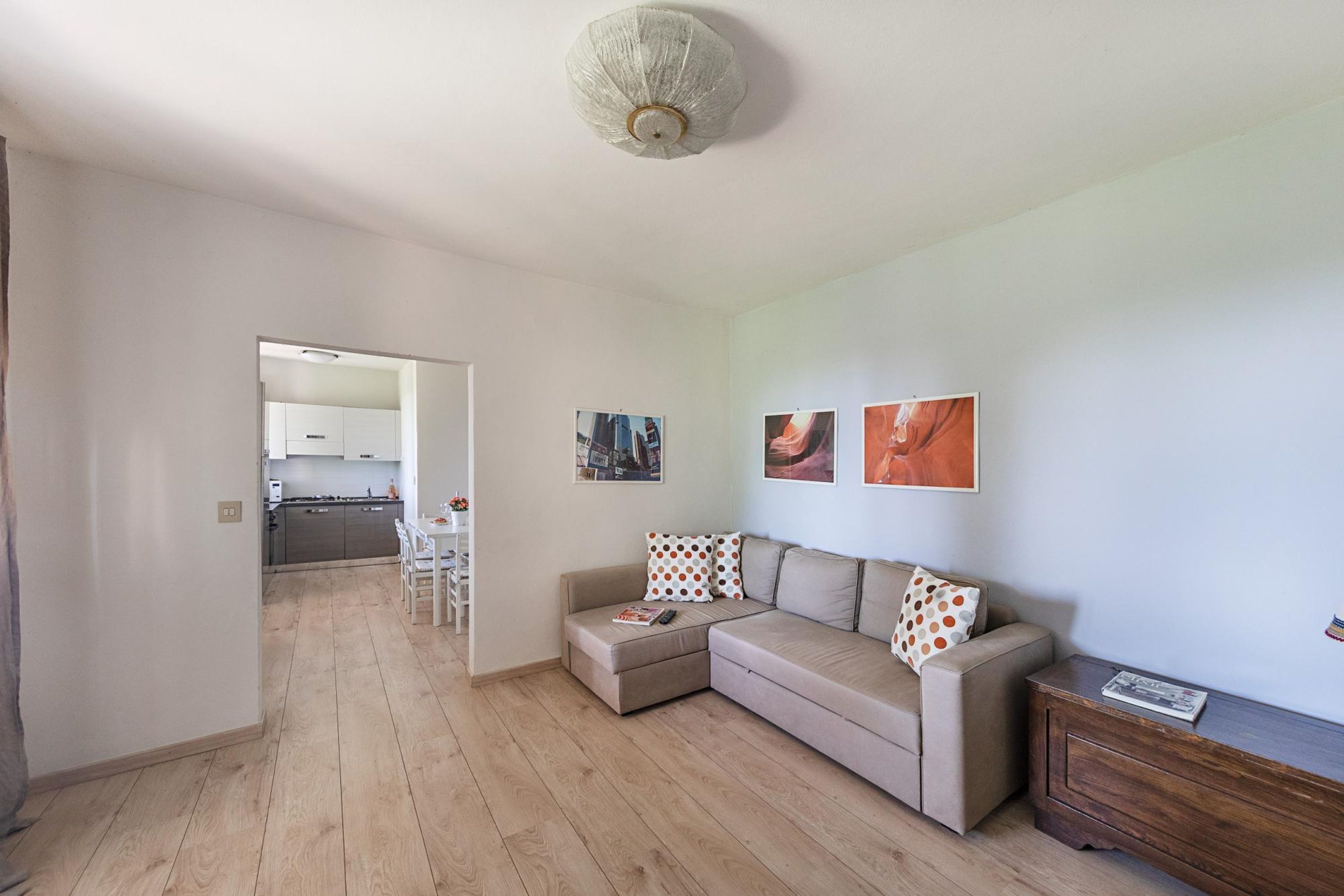 Un soggiorno moderno con un divano modulare beige, un pavimento in legno e una cucina sullo sfondo.