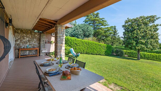 An outdoor dining area with a stone wall, a wooden bench, and a view of a well-maintained garden. - Casa Alba con Giardino e Patio by Wonderful Italy (Lonato del Garda)