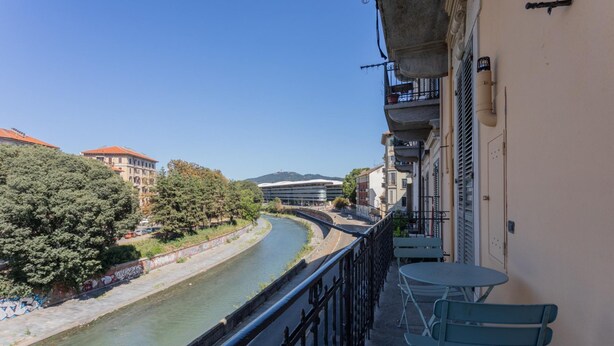 Un balcon avec vue sur une rivière, des arbres et des bâtiments.