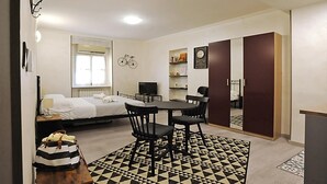 A compact hotel room with a bed, a desk with two chairs, a television, a bicycle decoration, and a bookshelf.