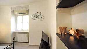 A room with a bed, a TV, a radiator, a window with curtains, and a wall-mounted bicycle.