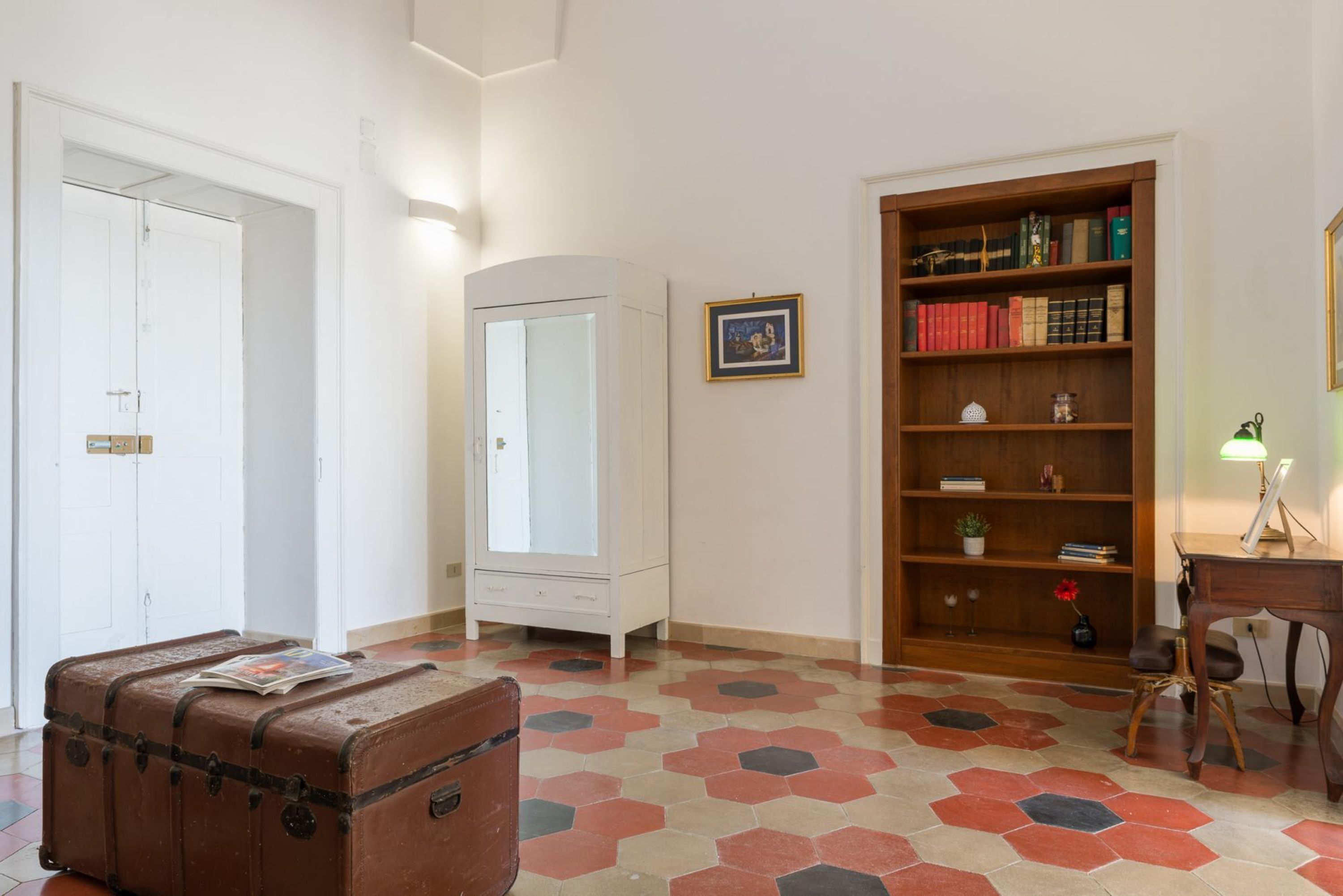 Una stanza con una grande libreria in legno, un armadio bianco, una valigia marrone e un pavimento decorato.