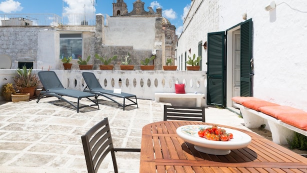 An outdoor patio with a table set for dining, a chair, and a lounge area with a bench and two sun loungers.