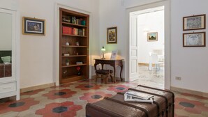A room with a large wooden bookshelf, a desk with a lamp, a chair, and a suitcase on the floor.