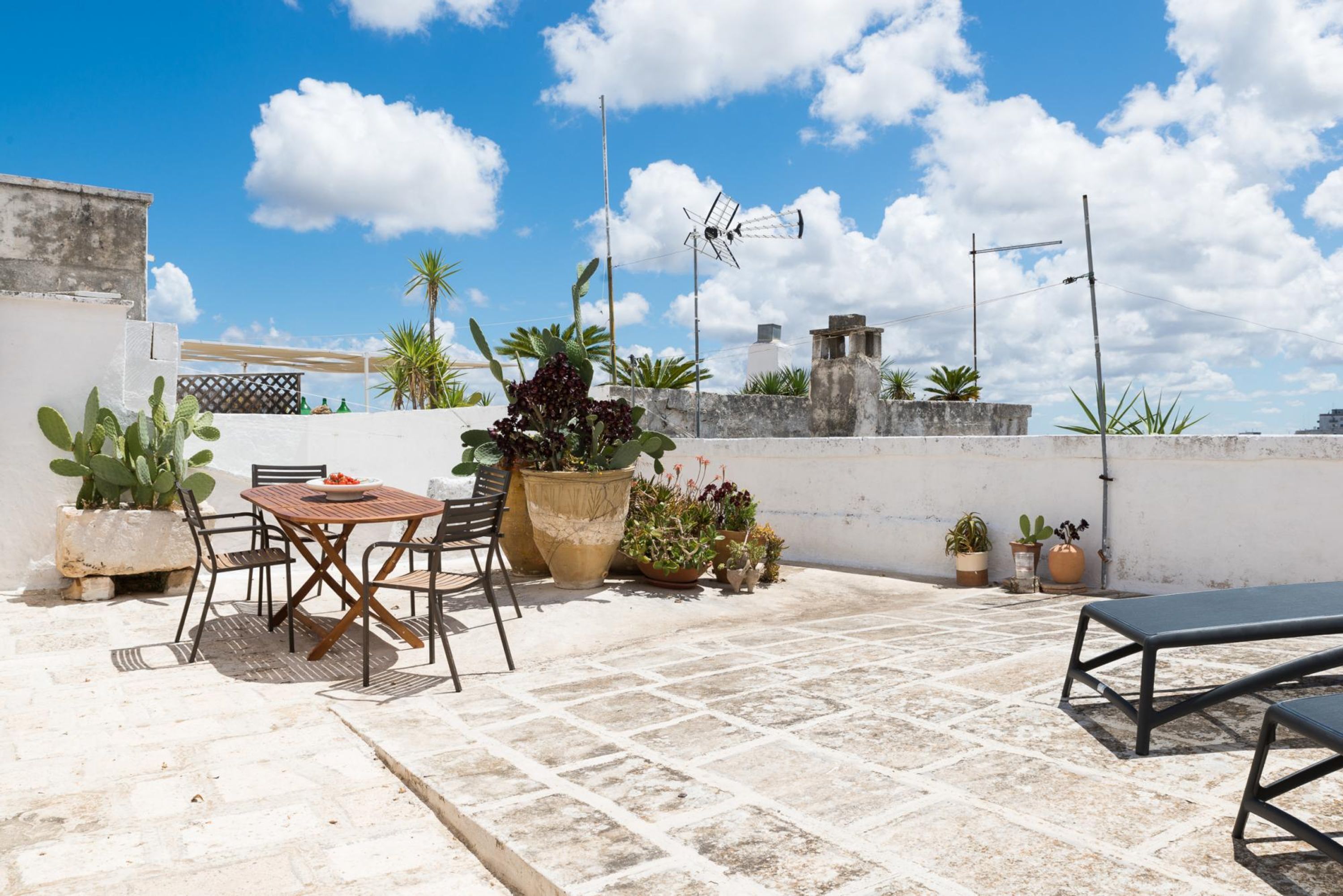 Eine Dachterrasse mit Tisch, Stühlen, Topfpflanzen und einem Windrad.