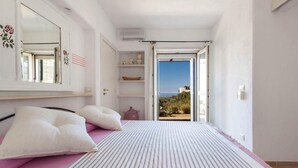 A bedroom with a bed, pillows, a shelf with decorative items, a mirror, and a view of the outdoors. - Relais Patriarca - Tirrenia - Utnz - IBR CAV (Ostuni)