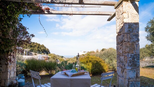 An outdoor dining area with a stone pillar, a table with chairs, and a view of the countryside. - Relais Patriarca - Tirrenia - Utnz - IBR CAV (Ostuni)