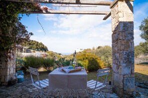Un área de comedor al aire libre con un pilar de piedra, una mesa con sillas y vistas al campo.