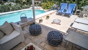 A poolside area with a sofa, ottomans, lounge chairs, and a table. - Relais Patriarca - Tirrenia - Utnz - IBR CAV (Ostuni)