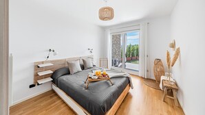 A modern bedroom with a large bed, bedside tables, a bedside lamp, a tray with breakfast, and a view of the outdoors. - Poggio al Sole 6 Apartment by Wonderful Italy (Toscolano Maderno)