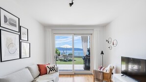 A modern living room with a sofa, TV, and a view of a balcony with outdoor furniture. - Poggio al Sole 6 Apartment by Wonderful Italy (Toscolano Maderno)