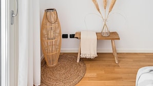 A minimalist room with a wooden floor, a woven floor mat, a wicker lamp, a small wooden table with a vase of pampas grass, and a straw hat on the wall. - Poggio al Sole 6 Apartment by Wonderful Italy (Toscolano Maderno)