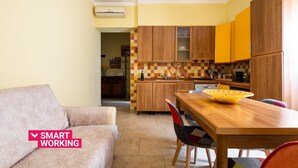 A compact kitchen with wooden cabinets, a dining table, and a sofa in a bright living area.