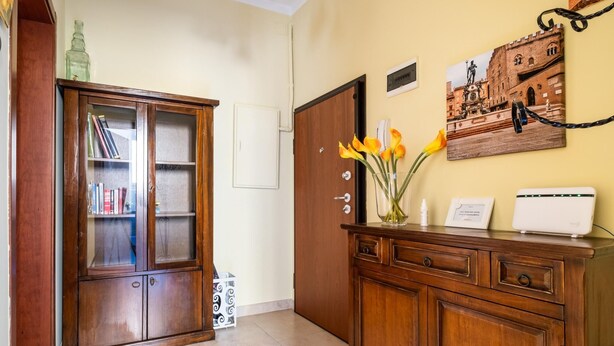 A wooden cabinet with glass doors, a white device on top, and a vase with flowers on a wooden dresser.