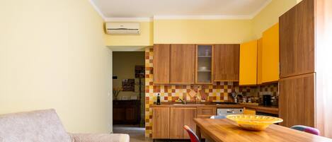 A compact kitchen with wooden cabinets, a dining table, and a sofa in a bright living area.