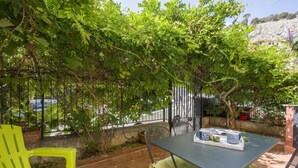 Eine Terrasse im Freien mit Esstisch, umgeben von Grünpflanzen und Blick auf die Straße.