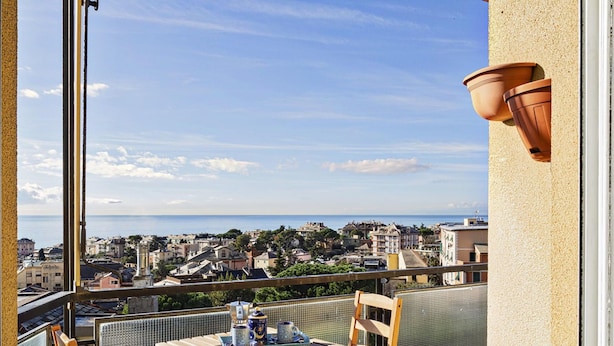 Un balcon donnant sur une ville côtière, une table avec des chaises et un pot en terre cuite accroché au mur.