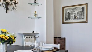 Un coin repas avec une table dressée pour quatre personnes, un lustre, un tableau historique encadré et un vase rempli de tournesols.