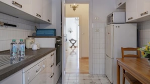 Une cuisine compacte avec des meubles blancs, un four à micro-ondes, un réfrigérateur et une table à manger en bois.