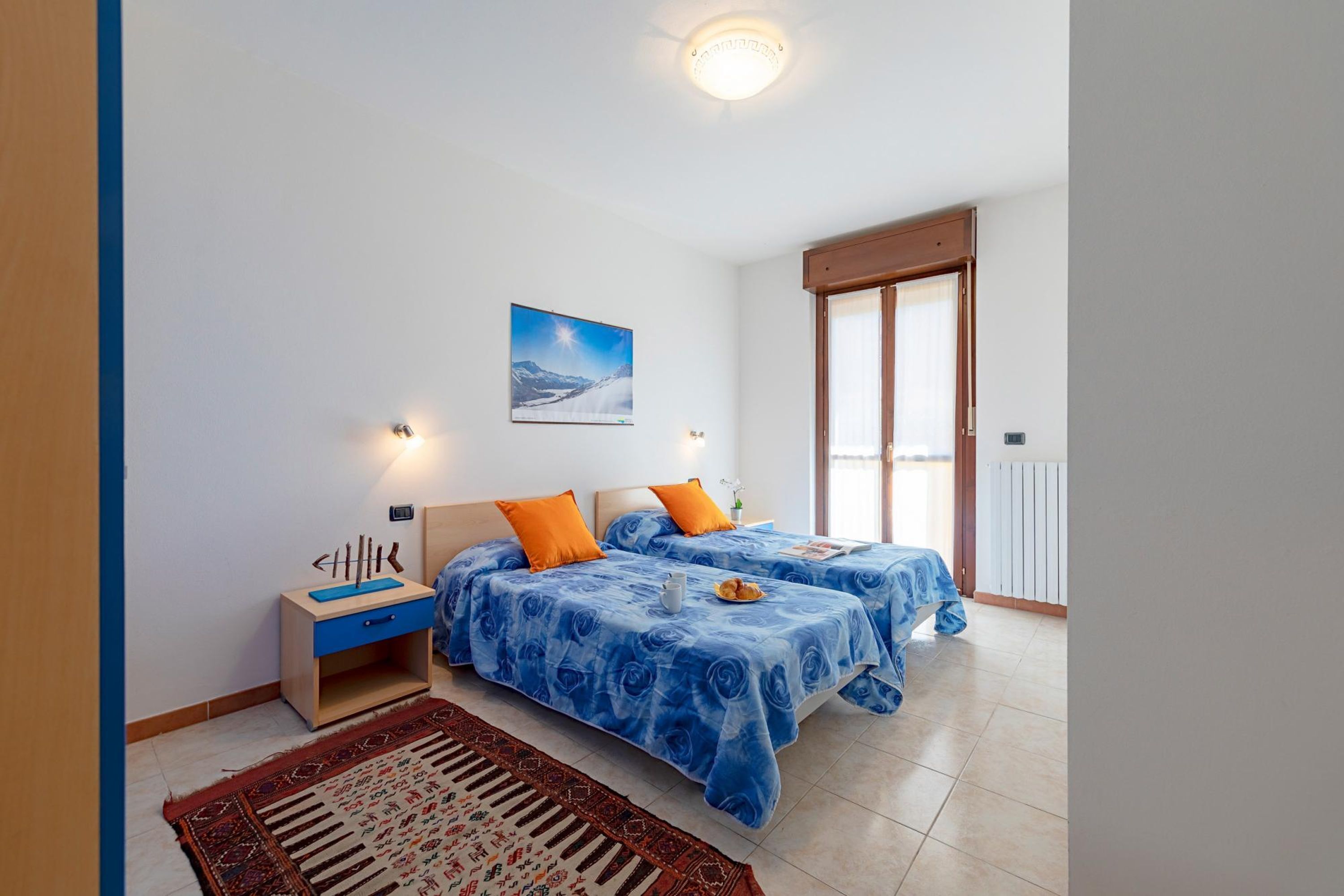 A bedroom with two beds, a nightstand, a rug, and a painting on the wall.