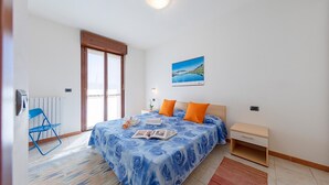 A bedroom with a bed, a nightstand, a chair, a window, and a picture on the wall.