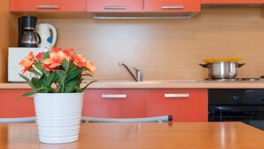 A kitchen with orange cabinets, a white coffee maker, a white pot on the stove, and a white vase with flowers on the counter.