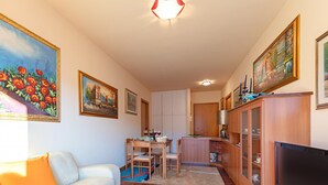 A living room with a sofa, a TV, a dining area with a table and chairs, and a kitchen area with cabinets and a refrigerator. - Kristall Lago 233 Apartment by Wonderful Italy (Desenzano del Garda)