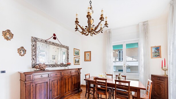 A dining room with a wooden table, chairs, a chandelier, and a large mirror on the wall. - I Fiori 3 16 Apartment by Wonderful Italy (Sanremo)