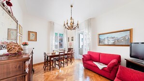 A living room with a red sofa, wooden floor, chandelier, dining table, and a painting on the wall. - I Fiori 3 16 Apartment by Wonderful Italy (Sanremo)
