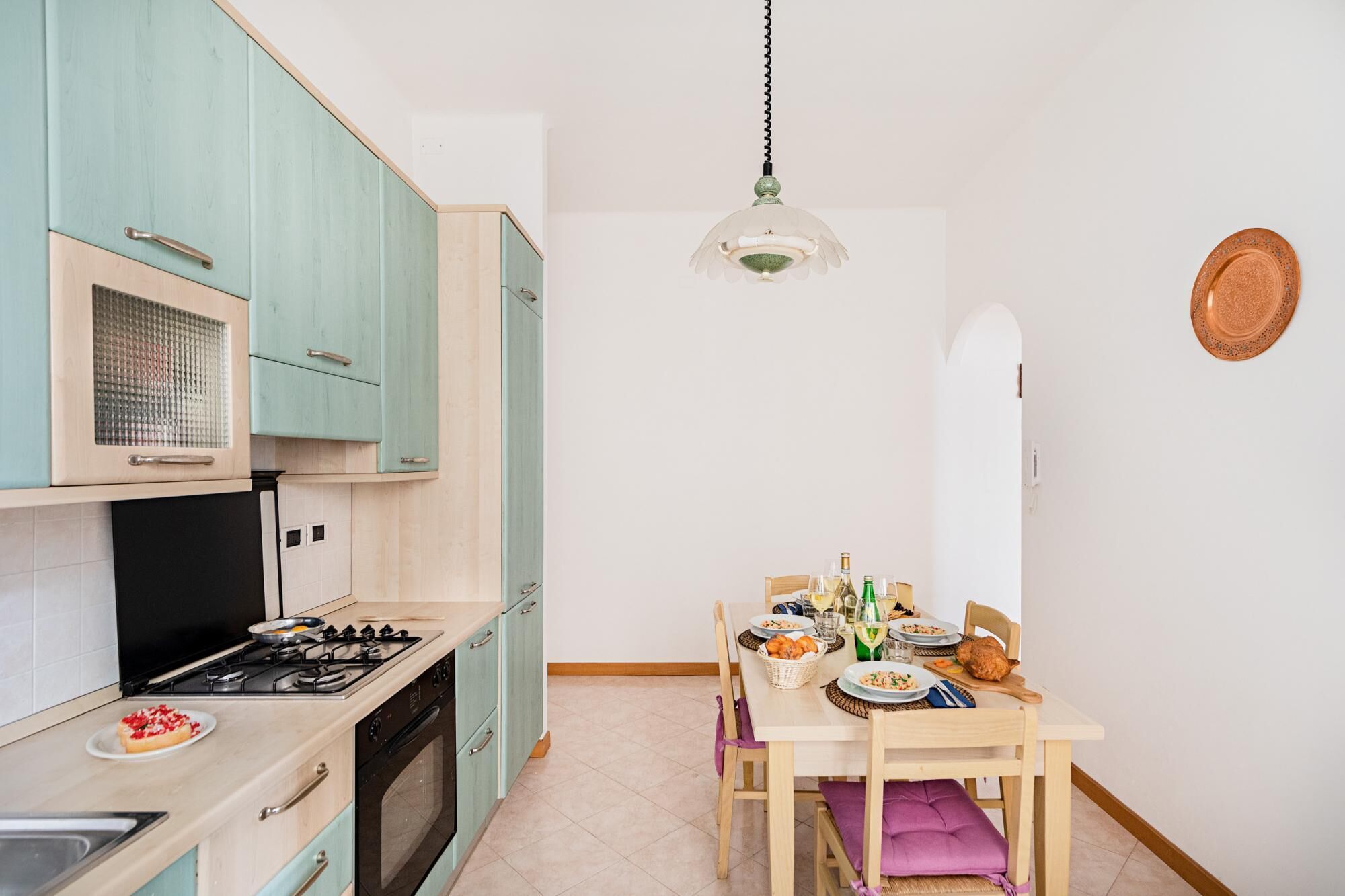 A kitchen with teal cabinets, a stove, and a dining table set with plates and glasses.