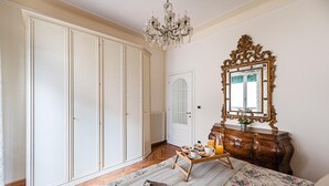 A bedroom with a large wardrobe, a dresser with a mirror, a breakfast tray, and a bed with a floral bedspread. - I Fiori 3 16 Apartment by Wonderful Italy (Sanremo)