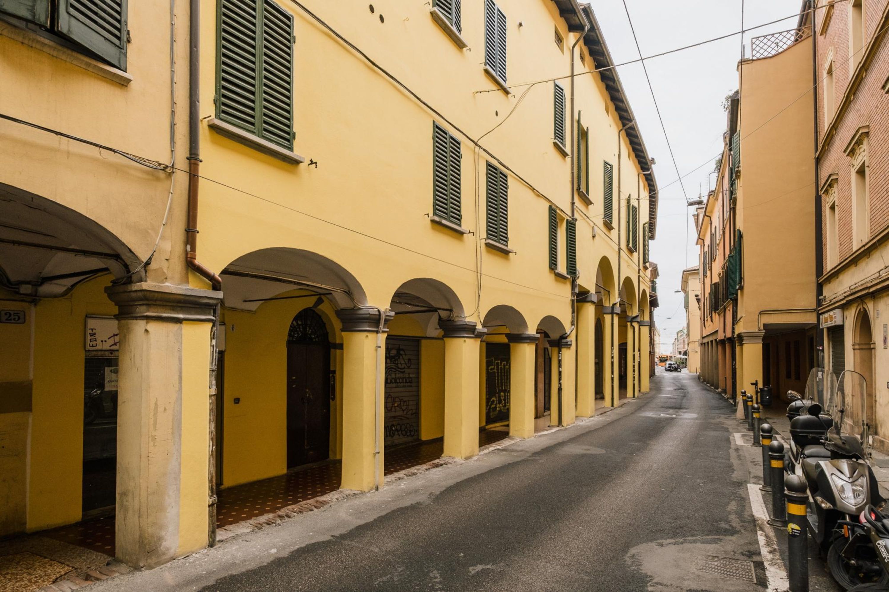 A narrow street lined with yellow buildings, some with arched doorways and shutters.