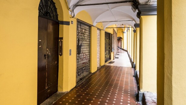 A corridor with yellow walls, a patterned floor, and a dark door with a metal gate.