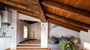 A spacious loft with exposed wooden beams, a kitchen with white cabinets, and a living area with a sofa and cushions.