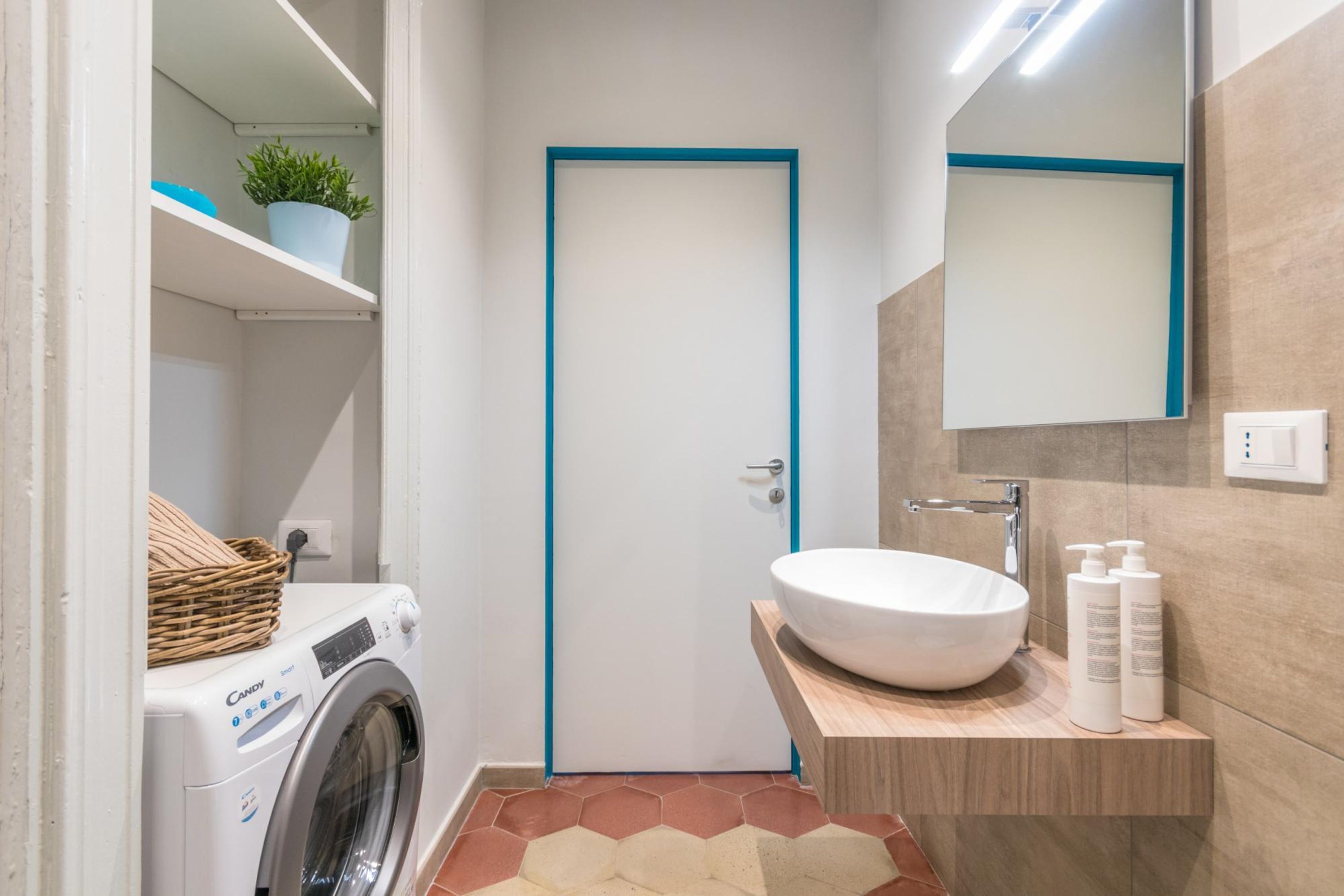 Een compacte badkamer met een wasmachine, een wastafel met een ruime wasbak en een spiegel boven de wastafel.