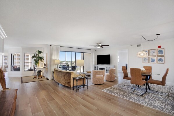 A spacious living room with a large TV, comfortable seating, and a dining area with a patterned rug.